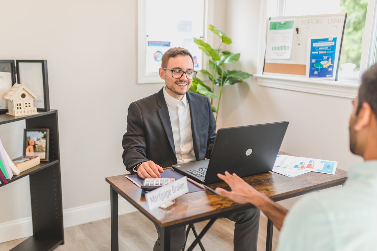 Services Mortgage broker in an office meeting with a client, utilizing a laptop.