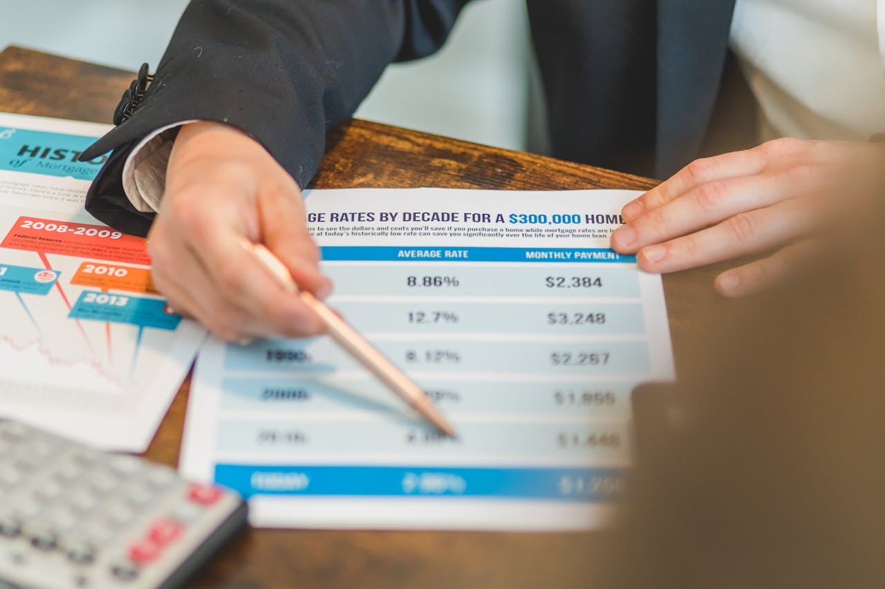 Services A close-up of hands analyzing mortgage rate documents with a pen and calculator in a business setting.